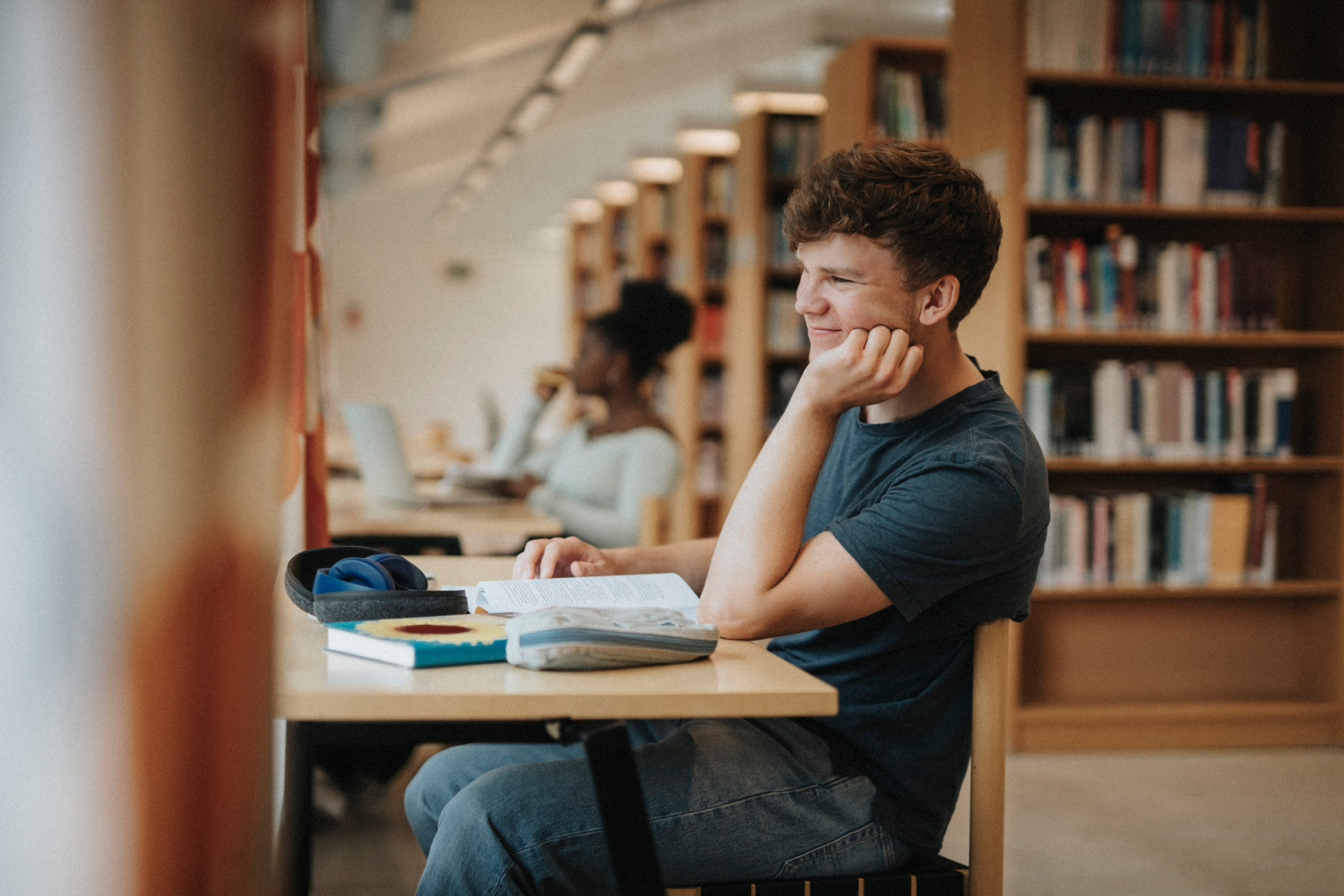 Ein Student, der an einem Schreibtisch mit Büchern und einem Laptop in einer Bibliothek lernt.