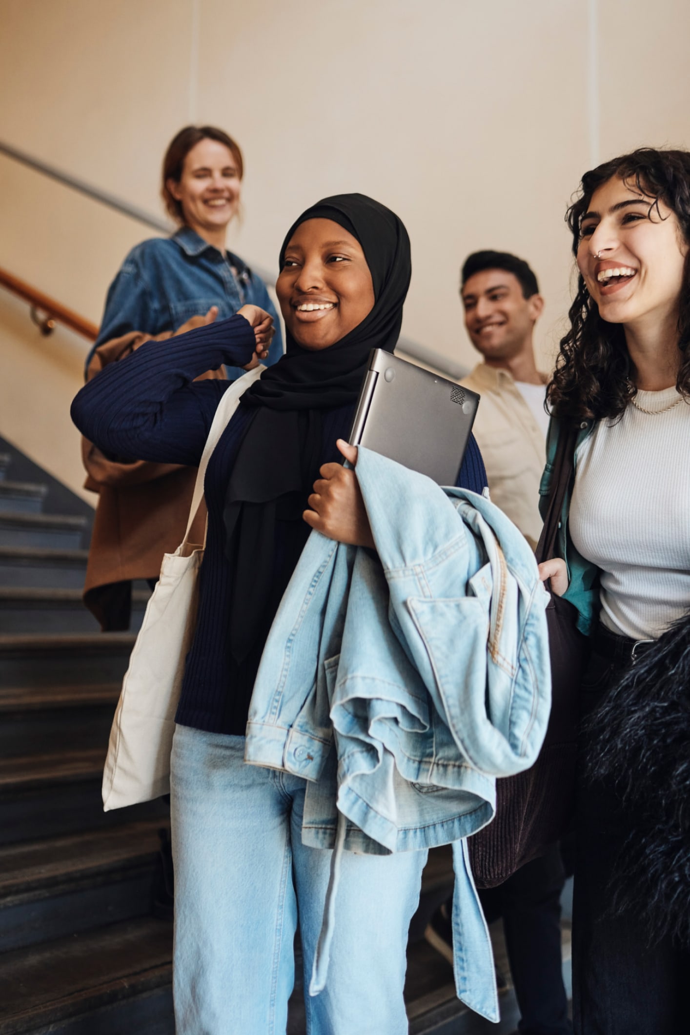 Eine lächelnde Frau mit Hijab hält einen Laptop, während sie die Treppe hinuntergeht
