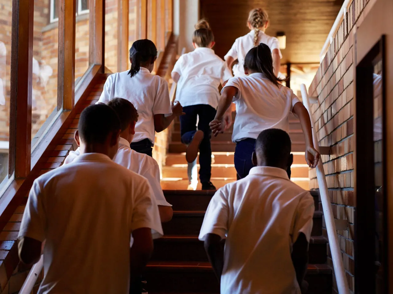 A group of students in matching white shirts hurry up a flight of stairs to get to class. 