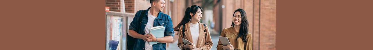 Three university students standing outside holding textbooks