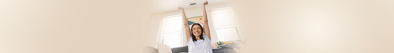 Female student sitting in front of laptop with arms raised and smiling
